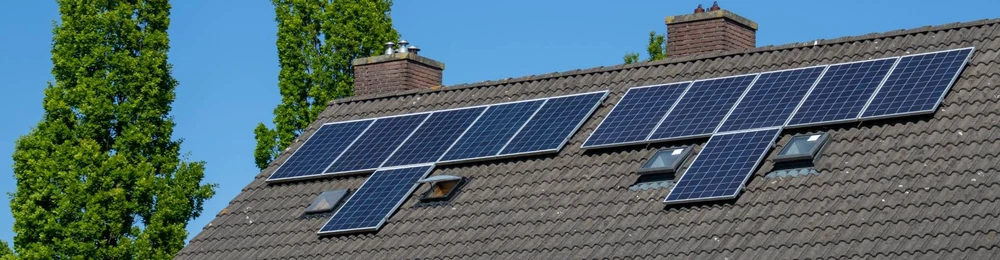 Toiture en tuiles grises d'une maison individuelle équipée de panneaux solaires photovoltaïques monocristallins bleu foncé, disposés en deux groupes asymétriques