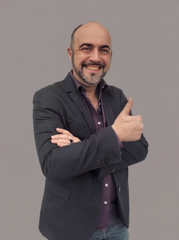 Portrait en studio du dirigeant de Voltaire Photovoltaïque, homme mature vêtu d'une chemise professionnelle bleue ou blanche, debout face caméra avec les bras croisés de manière naturelle et confiante, regard droit et sourire mesuré, fond neutre gris clair ou blanc, éclairage professionnel studio mettant en valeur une expression d'expertise et de fiabilité.